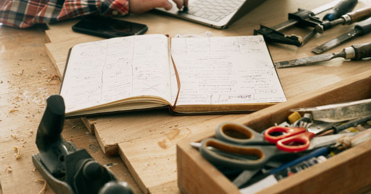 Un bureau de menuisier avec des outils, un carnet et un ordinateur portable, mettant en valeur la créativité et l'artisanat.